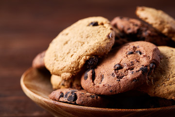 Side view of chocolate chip cookies on a wooden plate over rustic background, selective focus