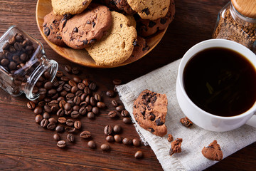 Coffee cup, jar with coffee beans, cookies over rustic background, selective focus, close-up, top view