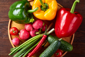 Wooden plate with vegetables for a vegetarian salad on rustic wooden background, close-up, selective focus