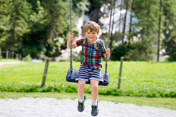 Funny kid boy having fun with chain swing on outdoor playground while being wet splashed with water