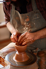 Close-up hands of a male potter in apron making a vase from clay, selective focus