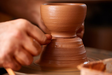 Close-up hands of a male potter in apron molds bowl from clay, selective focus