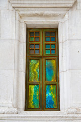 A window with colorful weathering in a white marble wall.