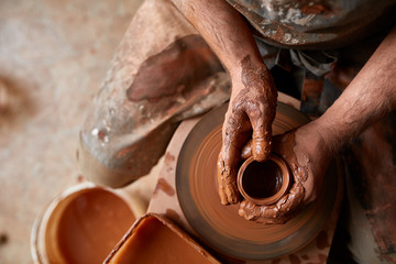 Close-up hands of a male potter in apron molds bowl from clay, selective focus