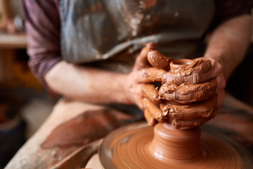 Close-up hands of a male potter in apron molds bowl from clay, selective focus