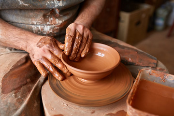 Close-up hands of a male potter in apron molds bowl from clay, selective focus