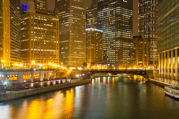 Yellow lights reflecting on the buildings and water of the Chicago River at night.