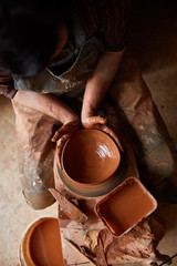 Close-up hands of a male potter in apron molds bowl from clay, selective focus