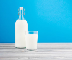 a glass of milk, a bottle of milk on a wooden table on a colored background