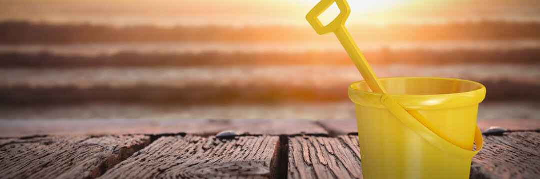Yellow bucket and shovel against image of a sunset over the waves