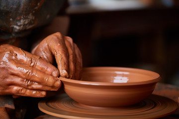 Close-up hands of a male potter in apron molds bowl from clay, selective focus
