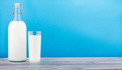 a glass of milk, a bottle of milk on a wooden table on a colored background