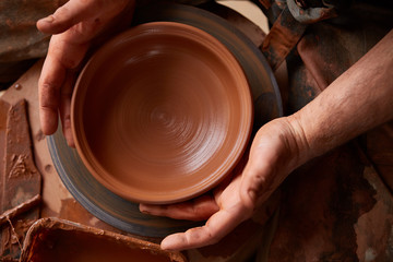 Close-up hands of a male potter in apron molds bowl from clay, selective focus
