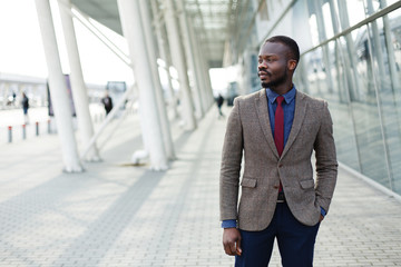 Stylish African American black businessman poses in a suit before a modern glass building outside