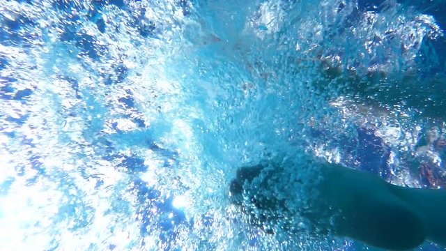 Man drops his feet in water in pool one by one. He tosses his feet in water. Bubbles of air. Rest on coast. Resort. Slow motion. Underwater shooting. Sunny day.