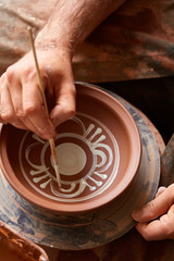 A potter paints a clay plate in a white in the workshop, top view, close-up, selective focus.