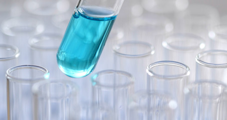 Science pipette with a drop of substance over laboratory test tubes