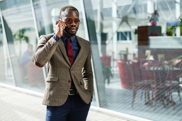 Stylish African American black businessman talks on his smartphone standing before a modern glass building outside