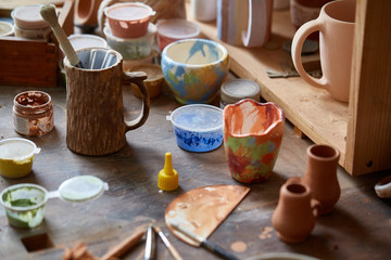 Close-up of various paint mugs and brushes in holder on worktop, selective focus, side view.