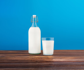 a glass of milk, a bottle of milk on a wooden table on a colored background