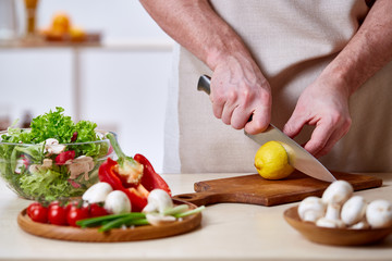 Man cooking at kitchen making healthy vegetable salad, close-up, selective focus.