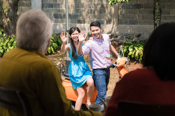 Cheerful young man and woman waving goodbye to their elderly parents after visiting them at home