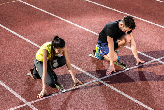 Male and female athlete in starting position at starting block of cinder track