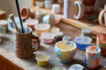 Close-up of various paint mugs and brushes in holder on worktop, selective focus, side view.