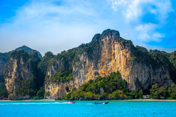 A thai long-tail boat and a motorboat racing along beautiful limestone mountains near Railay Beach in Krabi along the Andaman coast of Thailand.