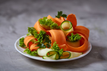 Artistically served vegetable salad with carrot, cucumber, letucce over white background, selective focus