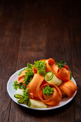 Artistically served vegetable salad with carrot, cucumber, letucce over wooden background, selective focus