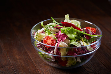 Fresh vegetable salad served in glass bowl over dark wooden background, selective focus, shallow depth of field