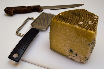 Piece of moldy old cheese, grater and big sharp knife on white cutting board and isolated on white...