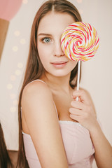 Cuty young blue eyes girl with candy is looking in camera in wonderful pink pajamas
