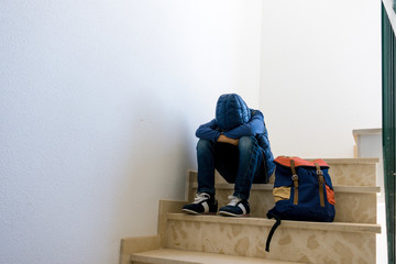 Sad boy with backpack sitting alone in the corner in the staircase