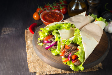 Photo of Mexican sandwich food, burrito, fajita, tacos, wrap made of tortilla, beef, chicken, fresh vegetables on rustic wooden background. Fast food concept. Healthy lunch snack. Copy space. 