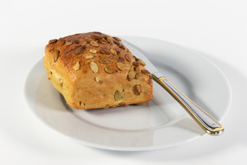 Kürbiskernbrötchen und Messer auf kleinem Teller isoliert auf weißem Hintergrund