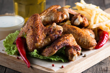 Close-up photo of bbq chicken wings with fries and beer. Barbeques meat with sauces, ketchup, mayonnaise. Fast and junk food concept. 