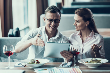 Smart man with tablet sits with young woman in cafe.