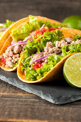 Photo of Mexican tacos with ground meat, beef, beans, onions and salsa on wooden background. Ketchup sauce and lime. A glass o beer in the background.