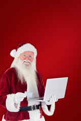 Santa pays with credit card on a laptop against red background