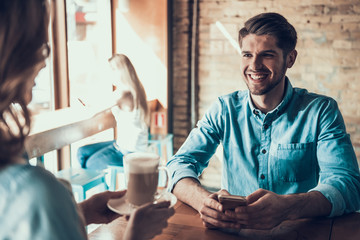 Happy man with phone sits in coffee shop with girl.