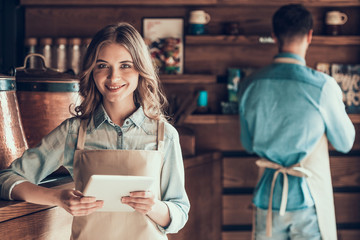 Portrait of beautiful barista in apron with tablet in cafe.