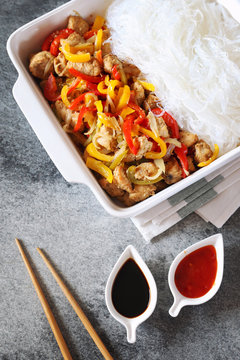 Asian food: fried chicken with tricolor bell peppers and rice vermicelli in ceramic crockery, soy sauce and chopsticks