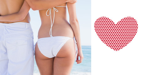 Rear mid section of fit couple facing the sea against valentines day pattern