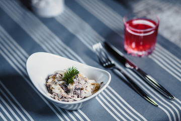 Table in the restaurant. On the table is a salad in a white plate, a knife, a fork, a glass with red juice. On the table is a blue tablecloth in strips.