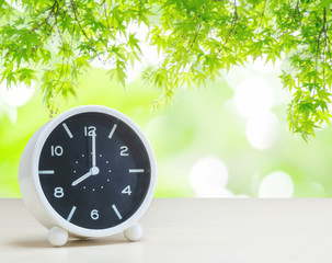 Closeup a table clock show the time  in 8 o'clock on white desk on blurred green leaves in garden view textured background