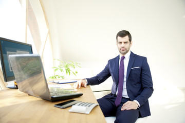 Businessman using laptop. Portrait of young financial assistant businessman wearing suit while sitting at office desk and working on financial report. 