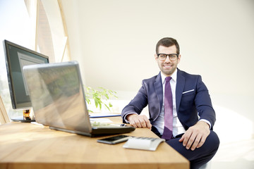 Businessman using laptop. Portrait of young financial assistant businessman wearing suit while sitting at office desk and working on financial report. 