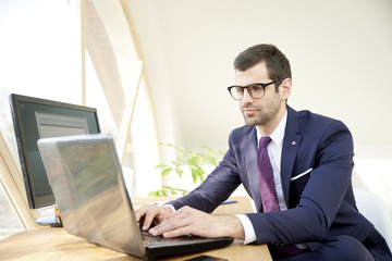Businessman using laptop. Portrait of young financial assistant businessman wearing suit while sitting at office desk and working on financial report. 